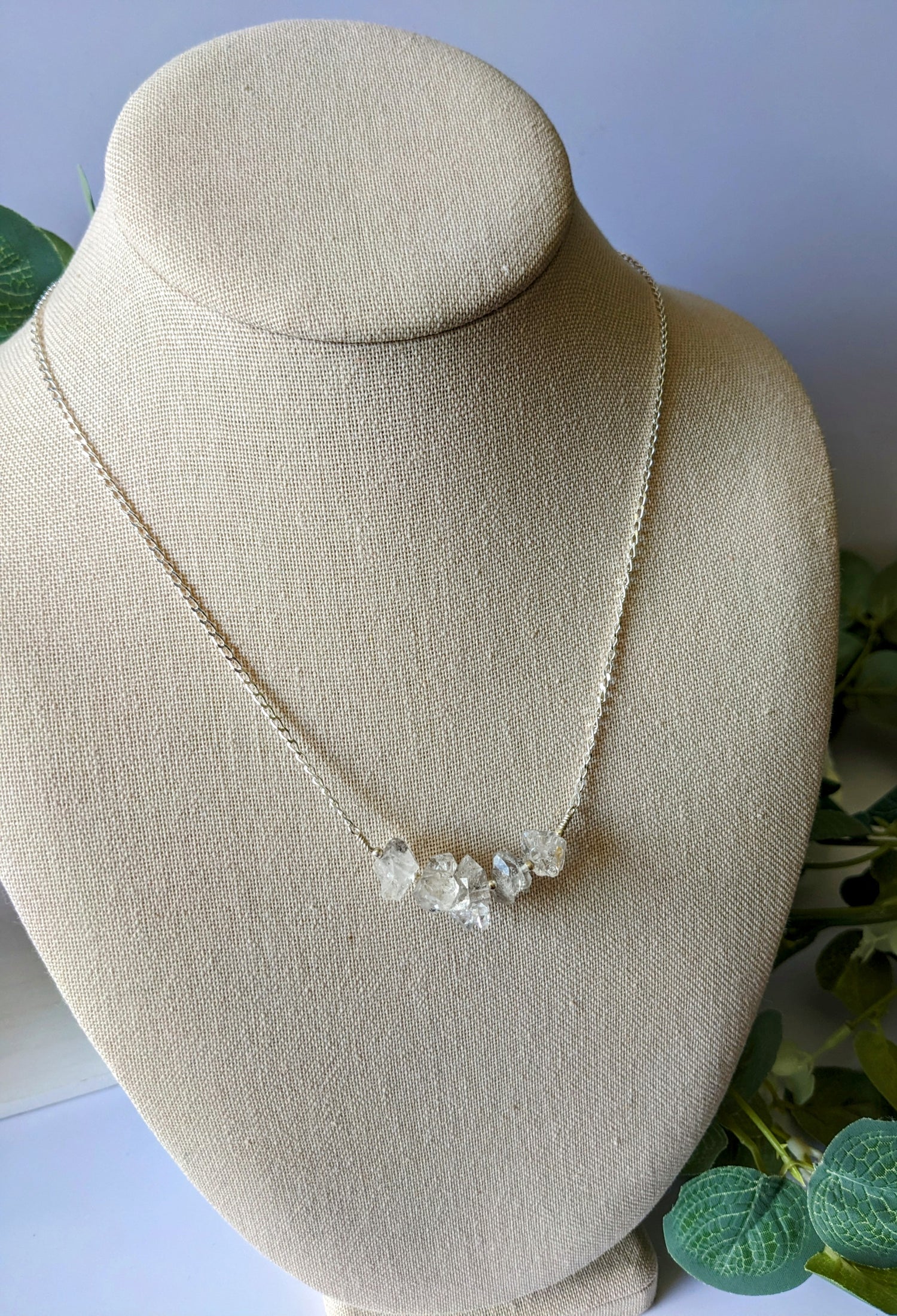 Sterling silver chain with five rough cut HERKIMER DIAMOND stones on a jewelry bust surrounded by greenery